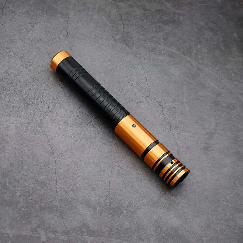 Jedi survivor twin lightsaber with black grip and golden accents on a textured surface.